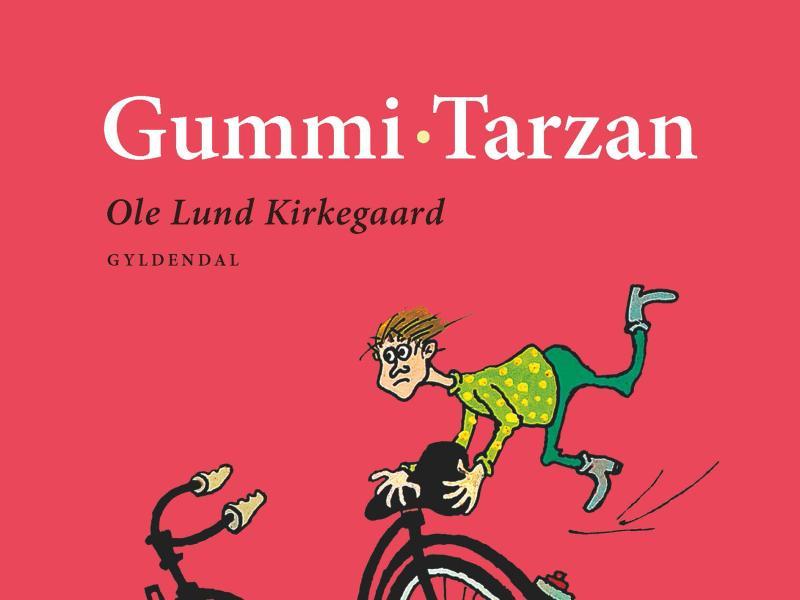 Det øverste af en ældre udgave af en Gummi-Tarzan bog. Baggrunden er rød, og man kan se den stakkels Gummi-Tarzan holde fast i sadlen på en cykel, mens den suser afsted